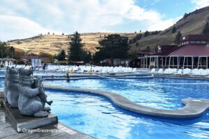 Kah-Nee-Ta Resort and Spa in Oregon: The picture "Kah-Nee-Ta Resort and Spa in Oregon pool with bear statues" features a sweeping outdoor pool with playful bear statues at the edge, white lounge chairs, and the resort buildings with sunlit hills in the background.