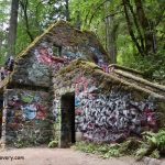 Witch's Castle Portland: Explore the Stone House in Forest Park - A moss-covered stone structure with colorful graffiti, surrounded by dense forest greenery and trees. The building has a staircase leading up to an elevated entrance