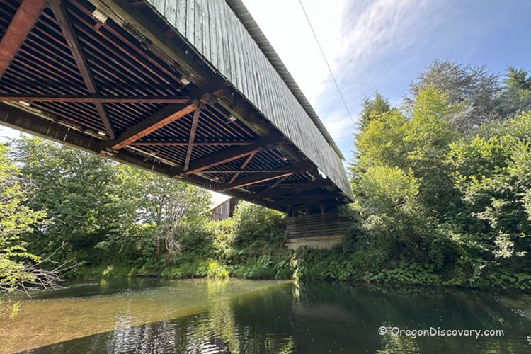 Hayden Covered Bridge Oregon Covered Bridge: View from below the covered bridge, showing its wooden trusses and the creek flowing underneath, surrounded by greenery.
