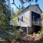 Belknap Covered Bridge in Oregon: The picture "Belknap Covered Bridge in Oregon entrance with road and weight limit sign" features the front entrance of the bridge, painted white, with a paved road leading inside, surrounded by tall trees and a weight limit sign on the right.