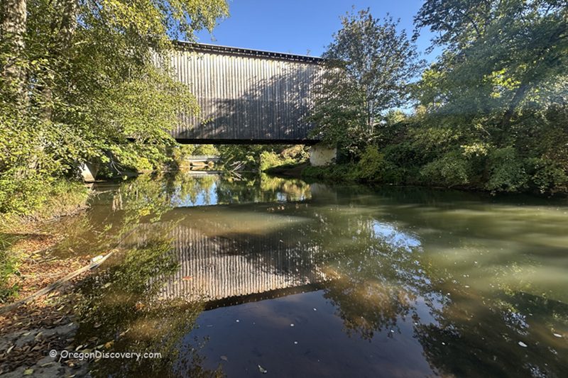 Chambers Covered Railroad Bridge in Oregon: The picture "Chambers Covered Railroad Bridge in Oregon bridge over river reflection" features the exterior of the covered bridge crossing a calm river, with the structure and surrounding trees reflected in the water below.
