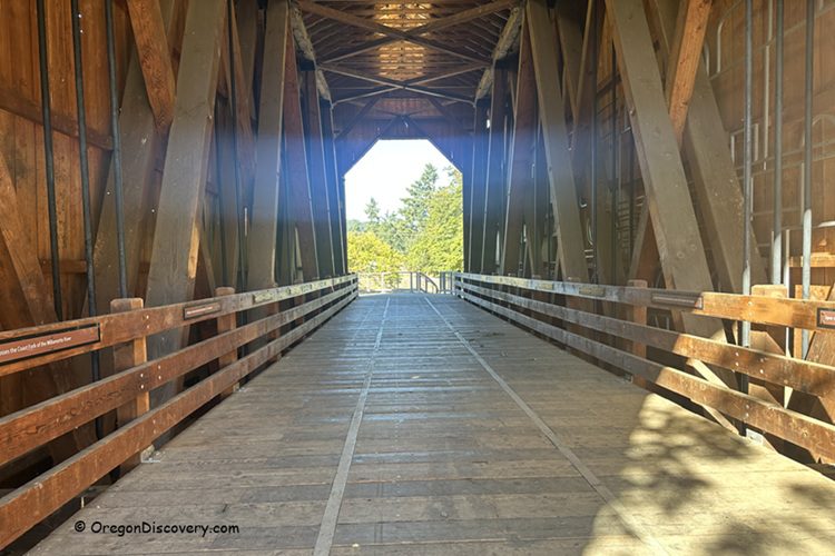 Chambers Covered Railroad Bridge in Oregon: The picture "Chambers Covered Railroad Bridge in Oregon wooden walkway interior" shows the inside of the historic covered bridge, with wooden planks and beams, looking straight through to the bright daylight and trees at the far end.