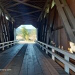 Parvin Covered Bridge in Oregon: The picture "Parvin Covered Bridge in Oregon interior wooden trusses" shows the inside of the covered bridge, with exposed wooden trusses and a plank floor, looking out to the bright landscape at the far end.
