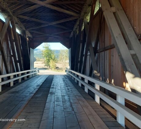 Parvin Covered Bridge in Oregon: The picture "Parvin Covered Bridge in Oregon interior wooden trusses" shows the inside of the covered bridge, with exposed wooden trusses and a plank floor, looking out to the bright landscape at the far end.