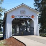 Weddle Covered Bridge in Oregon: The picture "Weddle Covered Bridge in Oregon festival banner entrance" shows the white wooden entrance to the bridge with a harvest festival banner above the opening, a black metal gate across the entrance, and trees on both sides.