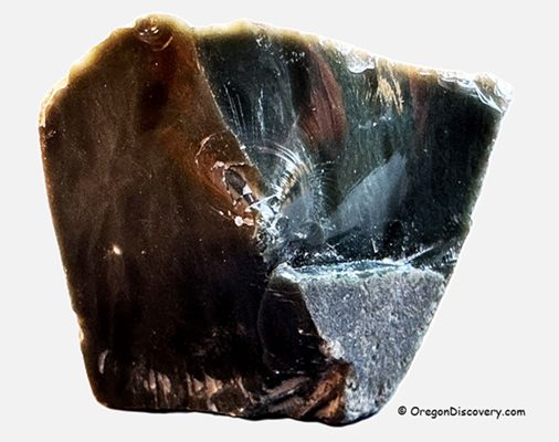 Mud Ridge at Burns - Oregon's Volcanic Glass: The picture "Mud Ridge at Burns obsidian specimen close-up" shows a detailed close-up of a glossy, dark brown to black piece of obsidian with sharp edges and reflective surfaces, highlighting the volcanic glass texture.