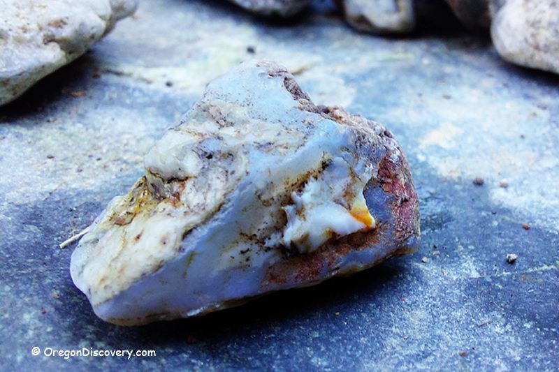 Quartzville Creek - Recreational Gold Panning and Rockhounding in Oregon: The picture "Quartzville Creek - close-up of chalcedony rock" shows a detailed close-up of a rough, pale blue and white chalcedony stone with hints of rust and dirt resting on a flat rock surface.