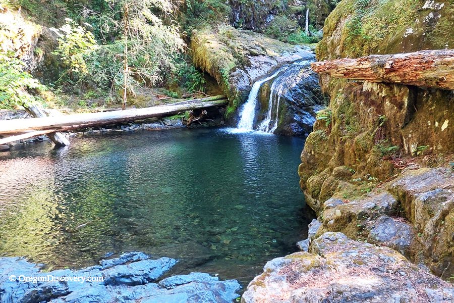 Blue Hole Falls on Brice Creek in Oregon: The picture "Blue Hole Falls waterfall and pool closeup" displays a close view of the waterfall cascading into the iconic deep blue-green pool, with mossy cliffs and fallen logs framing the clear, tranquil water.