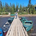 Olallie Lake in Oregon: The picture "dock with boats at shore" shows a wooden dock leading out into shallow water, with green rowboats and blue canoes tied up on both sides, and a person walking down the dock toward cabins and pine trees on the shore.