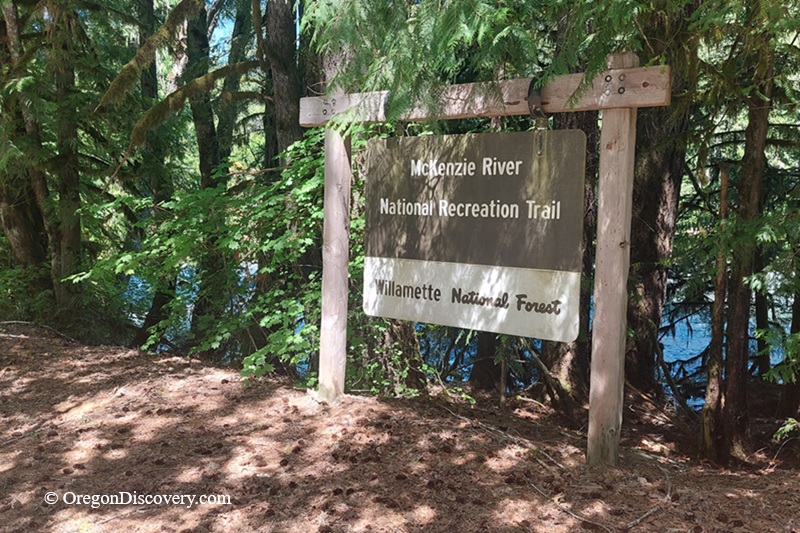McKenzie River Trail in Oregon: The picture "McKenzie River Trail entrance sign" features a large wooden sign reading "McKenzie River National Recreation Trail, Willamette National Forest," surrounded by tall green trees and with the river just visible behind.