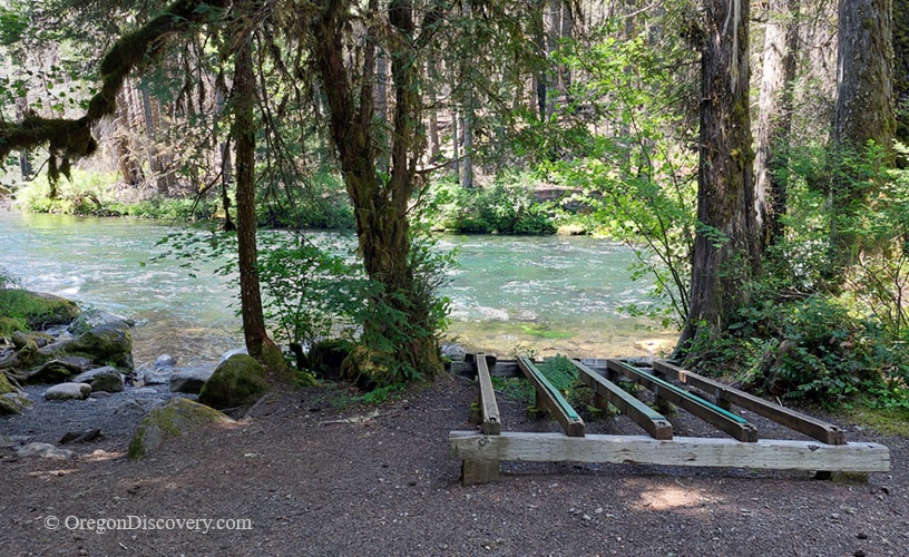 Olallie Campground in Oregon: The picture "Olallie Campground river access platform" features a wooden platform near the edge of a turquoise river, surrounded by lush vegetation and tall trees, providing convenient access to the water.