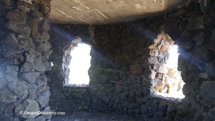 Dee Wright Observatory in Oregon – Dee Wright Observatory Stone Windows Dee Wright Observatory in Oregon – The picture "Dee Wright Observatory Stone Windows" shows the interior of the observatory with rough black lava stone walls and two arched windows letting beams of sunlight into the circular room.