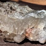 Rooster Rock Rockhounding in Oregon – Rooster Rock Agate Crystal Close-up Rooster Rock Rockhounding in Oregon – The picture "Rooster Rock Agate Crystal Close-up" shows a detailed view of a chunky agate and quartz crystal specimen with layered, translucent bands and mineral inclusions, resting on a sunlit surface.