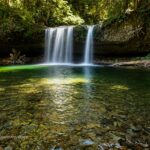Upper Butte Creek Falls Oregon – Upper Butte Creek Falls Long Exposure Upper Butte Creek Falls Oregon: The picture "Upper Butte Creek Falls Long Exposure" shows a long-exposure view of the waterfall, giving the falling water a silky effect as it pours into a vibrant green forest pool with a stony bottom and logs at the water’s edge.