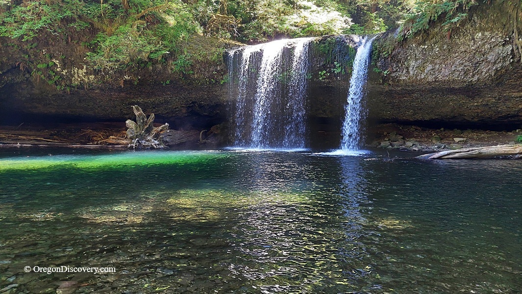 Upper Butte Creek Falls Oregon – Upper Butte Creek Falls Close View Upper Butte Creek Falls Oregon: The picture "Upper Butte Creek Falls Close View" centers on the twin streams of the waterfall, spilling over a mossy rock face into the clear, reflective plunge pool with green and blue hues, and forest growth along the rocky shore.